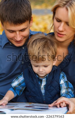 Cute little boy in autumn park with her parents read books. Happy family concept
