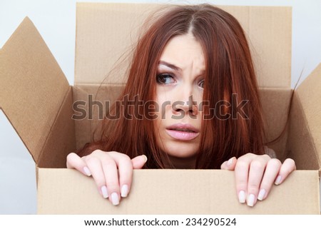 Beautiful girl looks out of a cardboard box. Difficult crossing concept. Emotions concept. Fear. Unexpected gift concept