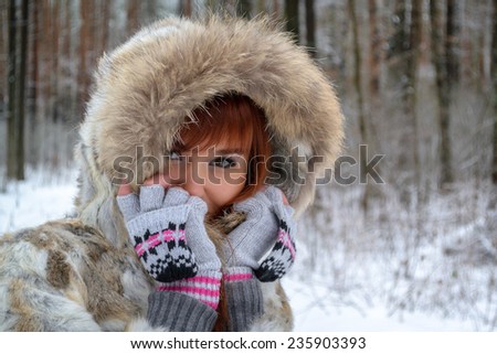 Portrait of beautiful red-haired girl in a fur coat and mittens in the winter forest