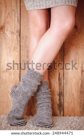 Legs of a woman in gray socks and gray sweater on the carpet on the wooden background