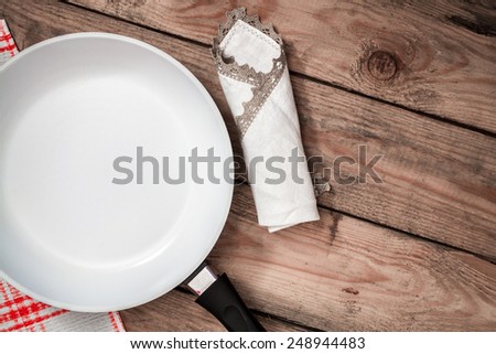Ceramic pan and kitchen napkin on old wooden table. top view