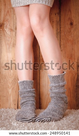 Legs of a woman in gray socks and gray sweater on the carpet on the wooden background