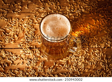 Glass of beer on old wooden table with grain. top view
