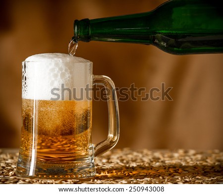 Pouring beer from a bottle into a glass on a wooden table with a grain