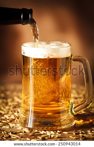 Pouring beer from a bottle into a glass. on brown background