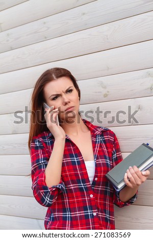 Portrait of unhappy student girl with books, talking on the phone