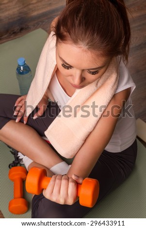 Beautiful sports girl does exercises with dumbbells sitting on a mat. top view