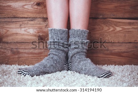 Legs of a woman in gray socks on the carpet on the wooden background.
