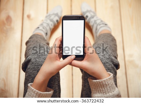 Girl with a phone in her hands sitting on the wooden floor.\top view