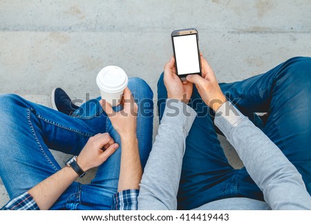 Two young men with the phone in his hand sitting on the steps. top view