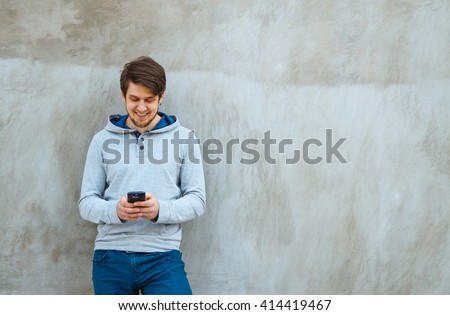 Young man writing sms standing by concrete wall. copy space
