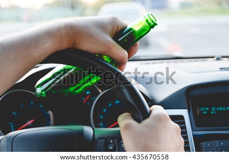 Drunk young man driving a car with a bottle of beer. Don\'t drink and drive concept. Driving under the influence. DUI, Driving while intoxicated. DWI