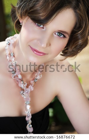 Young woman with pink make-up and green eyes in semi-precious stones necklace, late 20 - early 30