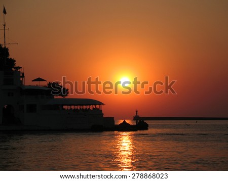Silhouette of a cafe on the waterfront of the Sevastopol harbor on the background of sea sunset with lighthouse. Sunset at Sevastopol harbor