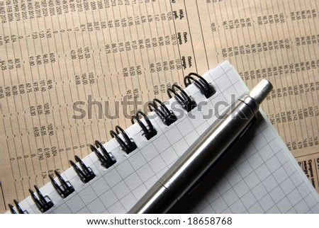 Pen and notebook laying on newspaper with financial data.