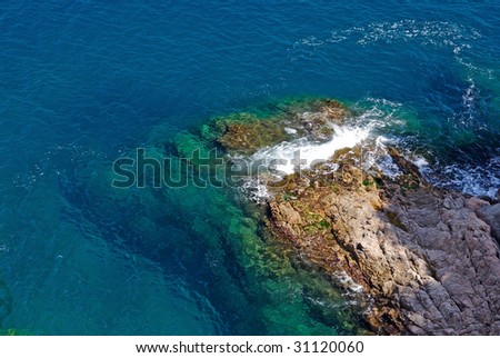 Rock in deep clean sea water. Seascape of Lloret de Mar shore, Spain.