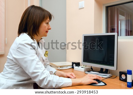 Woman roentgenographer at workplace in office clinic is browsing archives of digital images