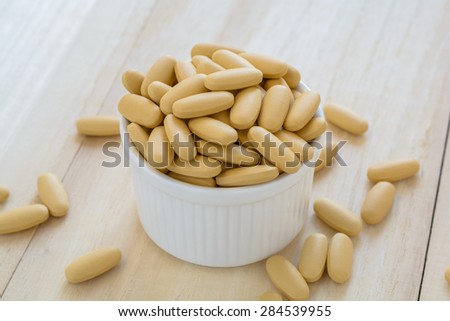 Brown pills in the white cup on the wooden background
