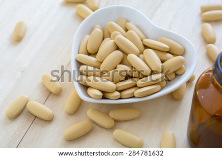 Brown pills in the white cup on the wooden background