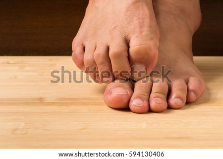 Close up a man with itchy feet uses his big toe to scratch his other foot on wooden floor.