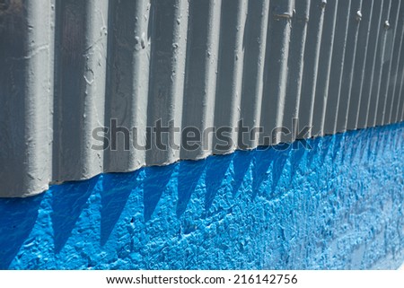 Abstract combination of light colored corrugated wall meeting foundation which is painted bright blue.