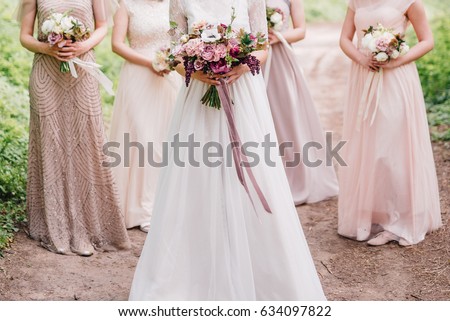 Bride and bridesmaid are holding bouquets of flowers in hands. Bridesmaid are on background. Wedding. Details.