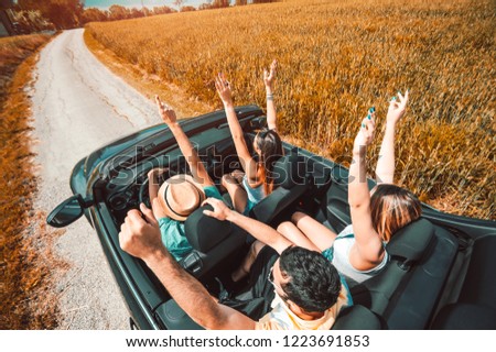 Group of happy friends having fun with hands up on a convertible car at roadtrip. Concept about transport, rental cars, people and lifestyle