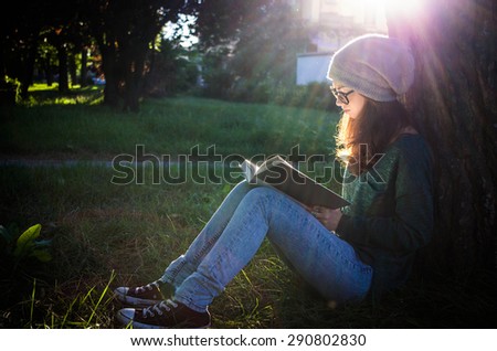 girl reading a book sitting in a park - people, nature and lifestyle concept
