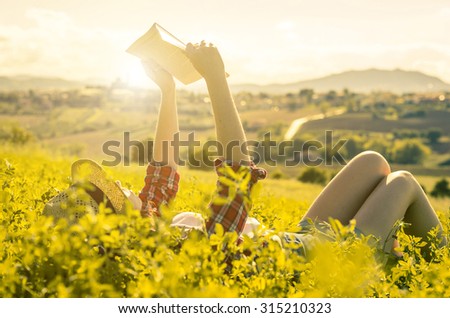girl reading a book lying on the grass - people, education, nature and lifestyle concept
