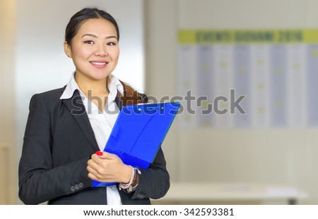 Attractive Asian businesswoman smiling and holding a folder in her office