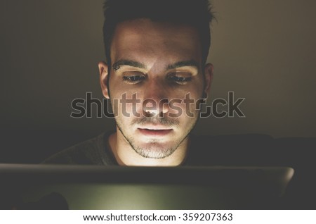 Young handsome man at laptop computer with light reflection from the screen to the face - technology, internet and people concept