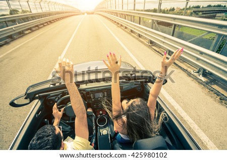 Happy couple driving on the road into the sunset in a sports car