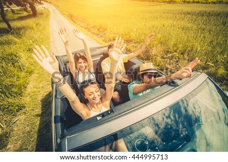Group of friends having fun at car trip. Four caucasian people on a sportive car with hands up.