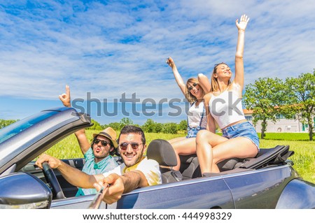Group of friends taking a selfie at car trip around Europe. Four caucasian people having fun on a sportive car outdoor.