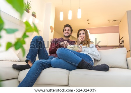 Couple having watching television eating pop corn on the sofa. Concept about television, lifestyle, people and having fun