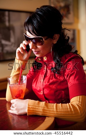 Young pretty girl is calling to somebody while drinking cocktail