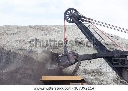 A haul truck is being loaded with dirt and ore at a mine site while another haul truck waits in the foreground.