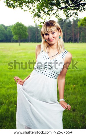Portrait of a smiling white girl in white dress against the background of the summer foliage