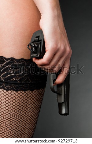 Female hand with a gun on a dark background in stockings