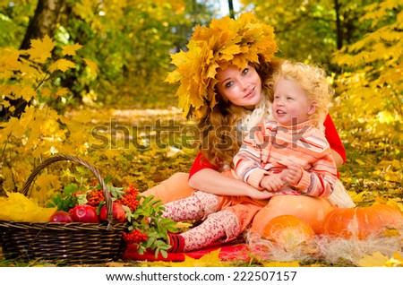 Young red-haired mom holding a child on a picnic in the autumn park with a wreath of yellow leaves on the head
