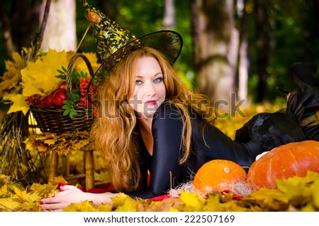 Beautiful young red-haired witch in the autumn forest on a holiday Halloween