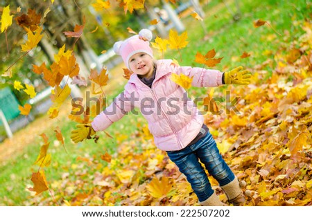 Beautiful little girl throws up yellow autumn leaves in the park