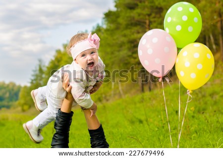 Mother throws up in the air laughing little girl on picnic in the park. Birthday celebration and balloons.