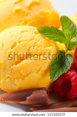 Scoops of yellow ice cream with raspberries and chocolate curls