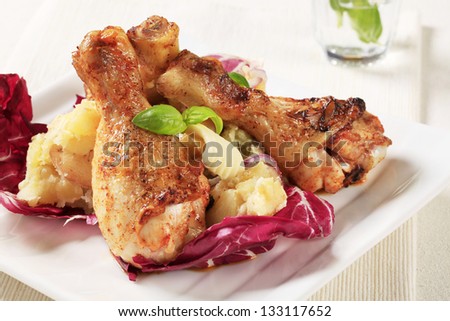 Roasted chicken legs on mashed potatoes with fried onion on a red cabbage leaf