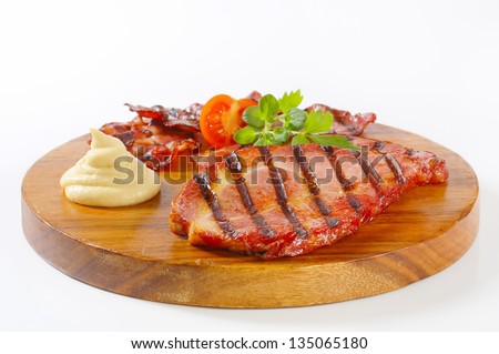 Slices of grilled pork neck and strips of crunchy bacon on a round cutting board