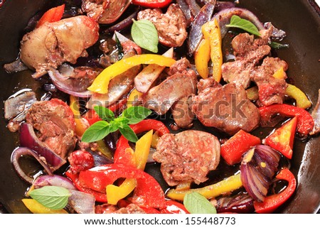 Roasted goose liver with fried onion and bell pepper in a black pan