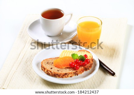 Bread with butter and fruit, cup of tea and orange juice