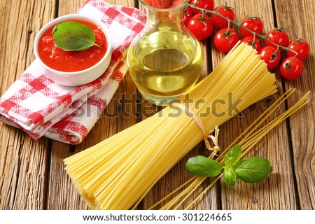Still life of dried spaghetti, tomato puree and olive oil on wooden background