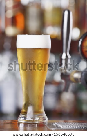 Schooner glass of Ice Cold Beer sitting on bar top near beer pouring tap